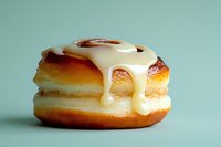 Glazed cinnamon roll with white icing dripping down sides on mint green background. Fresh baked pastry dessert for bakery menu and food photography projects.