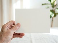 Mature adult hand holding blank white card mockup for business branding, greeting design, or promotional messaging in bright interior setting.
