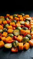 Roasted autumn vegetables with Brussels sprouts, butternut squash cubes and red bell peppers in cast iron pan for healthy seasonal cooking and meal prep.