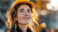 Professional female construction worker in yellow hard hat smiling confidently at construction site with warm golden hour lighting and bokeh background.