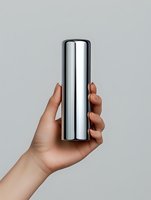 Cropped hand holding shiny metallic cylindrical container against neutral background, isolated on white for product mockup, packaging design, and commercial advertising use.