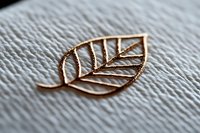 Delicate rose gold leaf outline on textured white paper background showcases minimalist jewelry design element with intricate vein pattern detail.