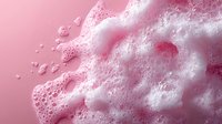 Pink foam bubbles with soft delicate texture on pastel background, macro photography showing detailed soap suds and frothy liquid surface in cosmetic style.