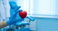 Medical professional in blue gloves holding red heart symbol in hospital setting representing cardiology care and cardiovascular health treatment.