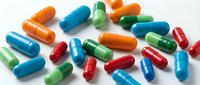 Colorful pharmaceutical capsules scattered on white background showing various medications in blue, orange, green and red colors for healthcare design.