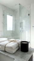 Modern bathroom with marble shower enclosure, white rolled towels tied with twine, and black candle on marble countertop. Spa and wellness design.