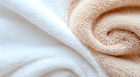 Soft white and beige cotton towels in spiral fold pattern creating abstract texture background, close-up view showing fabric detail and gentle curves.