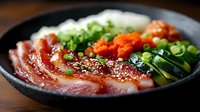 Fresh raw tuna sashimi bowl with green onions, sesame seeds, cucumber and carrots served in traditional black ceramic plate on wooden surface.