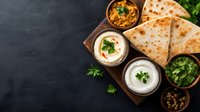 Traditional Indian quesadillas served with fresh cilantro, spicy curry sauce and white yogurt dips on dark wooden board against black background. Food photography.