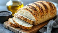 Freshly baked poppy seed bread loaf sliced on wooden cutting board with olive oil and seeds in background, ideal for breakfast or sandwich making.