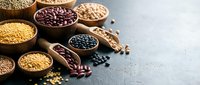 Assorted legumes and grains in wooden bowls on gray surface, including lentils, beans, and pulses for cooking and nutrition.