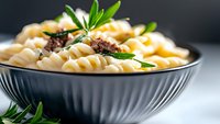 Creamy fusilli pasta with ground meat sauce garnished with fresh rosemary in gray ceramic bowl on light background, close up view of traditional Italian cuisine.