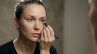 Caucasian woman in her 30s applying eyeliner pencil while looking in mirror, beauty routine and makeup application concept.