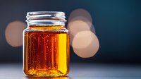 Glass jar filled with golden honey or maple syrup on dark background with soft bokeh lights, minimalist food photography composition for packaging design.