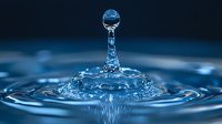 Mesmerizing water drop collision creating crown splash formation with suspended droplet above, captured in high-speed macro photography against dark blue background.