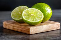 Fresh cut limes on wooden cutting board against dark background, close up view showing juicy citrus texture and bright green color for food and drink concepts.
