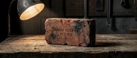 Vintage industrial brick with embossed text on weathered wooden surface under warm lamp light creating atmospheric workspace decor for rustic interior design.