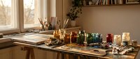 Artist workspace with watercolor paints, brushes and art supplies on wooden table near window. Creative studio setup for painting and drawing projects.