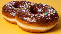 Chocolate glazed donuts with colorful sprinkles on bright yellow background. Fresh baked pastries with rich dark chocolate coating and rainbow sugar decorations.