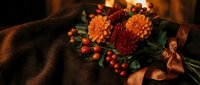 Autumn bouquet with orange chrysanthemums and red berries on cozy brown fabric background. Seasonal floral arrangement for fall decorating and holidays.