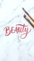 Pink calligraphy lettering spelling beauty with makeup brushes and cosmetics on marble surface for design projects.