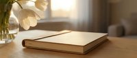 Elegant notebook on wooden table with white tulips in vase, warm golden sunlight streaming through window, cozy home office setting.