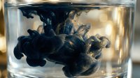 Dark ink swirling and dispersing in clear water creating abstract fluid patterns in glass container for creative design projects.