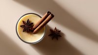 Creamy eggnog cocktail with cinnamon sticks and star anise on beige background with soft shadows, perfect for holiday menu design.