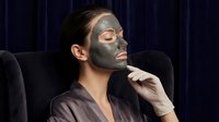 Young man relaxing with gray clay facial mask in spa chair for skincare routine and wellness treatment at home.