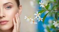 Young woman with glowing skin touching face near blooming jasmine flowers. Natural skincare and beauty concept with fresh botanical elements.