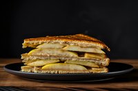 Grilled cheese sandwich with melted cheese on toasted bread served on black plate against dark background for food photography and culinary content.