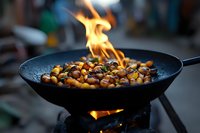 Roasted chestnuts and corn kernels flambéing in cast iron pan over open flame, creating dramatic cooking scene with bright orange fire and dark background.