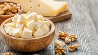 Fresh cubed feta cheese in wooden bowl with walnuts and cheese block on rustic wooden table background, traditional Mediterranean dairy product.