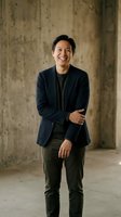 Happy Asian businessman in navy blazer laughing confidently in modern concrete office space for corporate marketing and professional branding materials.