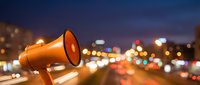 Orange megaphone against blurred city lights at dusk with bokeh traffic and urban nightscape for communication and announcement campaigns.