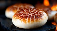 Freshly baked artisan bread rolls with golden crosshatch pattern on dark slate surface near warm fireplace creating cozy bakery atmosphere for culinary content.