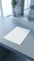 Blank white paper sheet on modern office desk with natural lighting and plant in background for business presentations and documents.