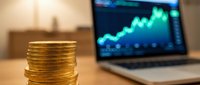 Stack of golden coins with laptop displaying upward trending financial chart in background, representing investment growth and financial success.