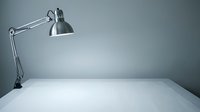 Adjustable metal desk lamp with articulated arm positioned above empty white surface against gray background, suitable for workspace and office design projects.