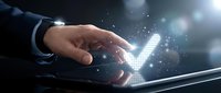 Businessman hand touching glowing digital checkmark symbol with sparkling light effects on dark background for approval and success concepts.