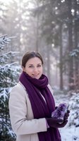 Smiling Caucasian woman in beige coat and purple scarf holding snow in winter forest with soft sunlight filtering through snowy trees.