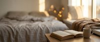 Cozy bedroom interior with open book and coffee cup on wooden surface, soft morning sunlight streaming through window creating warm atmosphere for relaxation.