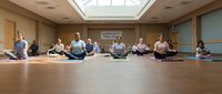 Group of diverse people practicing meditation in modern wellness studio with natural lighting and wooden floors for mindfulness training.