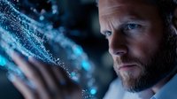 Bearded man interacting with glowing blue digital particles, side profile view in dark environment with futuristic technology visualization and bokeh effects.