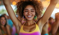 Young African American woman with natural curly hair and glasses expressing joy with arms raised, wearing colorful tank top and hoop earrings, genuine smile against blurred background.