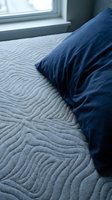 Dark blue pillow resting on quilted gray bedding near a bright window, showcasing bedroom decor and comfortable sleep setup for home design and lifestyle content.