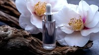 Luxury skincare serum bottle with dropper on driftwood beside white peony flowers for natural beauty and wellness cosmetic product photography.