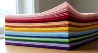 Stack of colorful felt fabric sheets arranged in rainbow order on wooden surface. Craft materials for DIY projects, sewing, and creative activities.