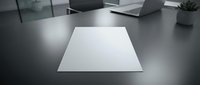 Clean white paper sheet on modern office desk with laptop and plant in blurred background. Minimalist workspace setup for business presentations and documents.