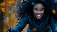Young African American woman with natural curly hair and bright smile enjoying autumn outdoors, wearing black coat against blurred golden fall foliage background.
